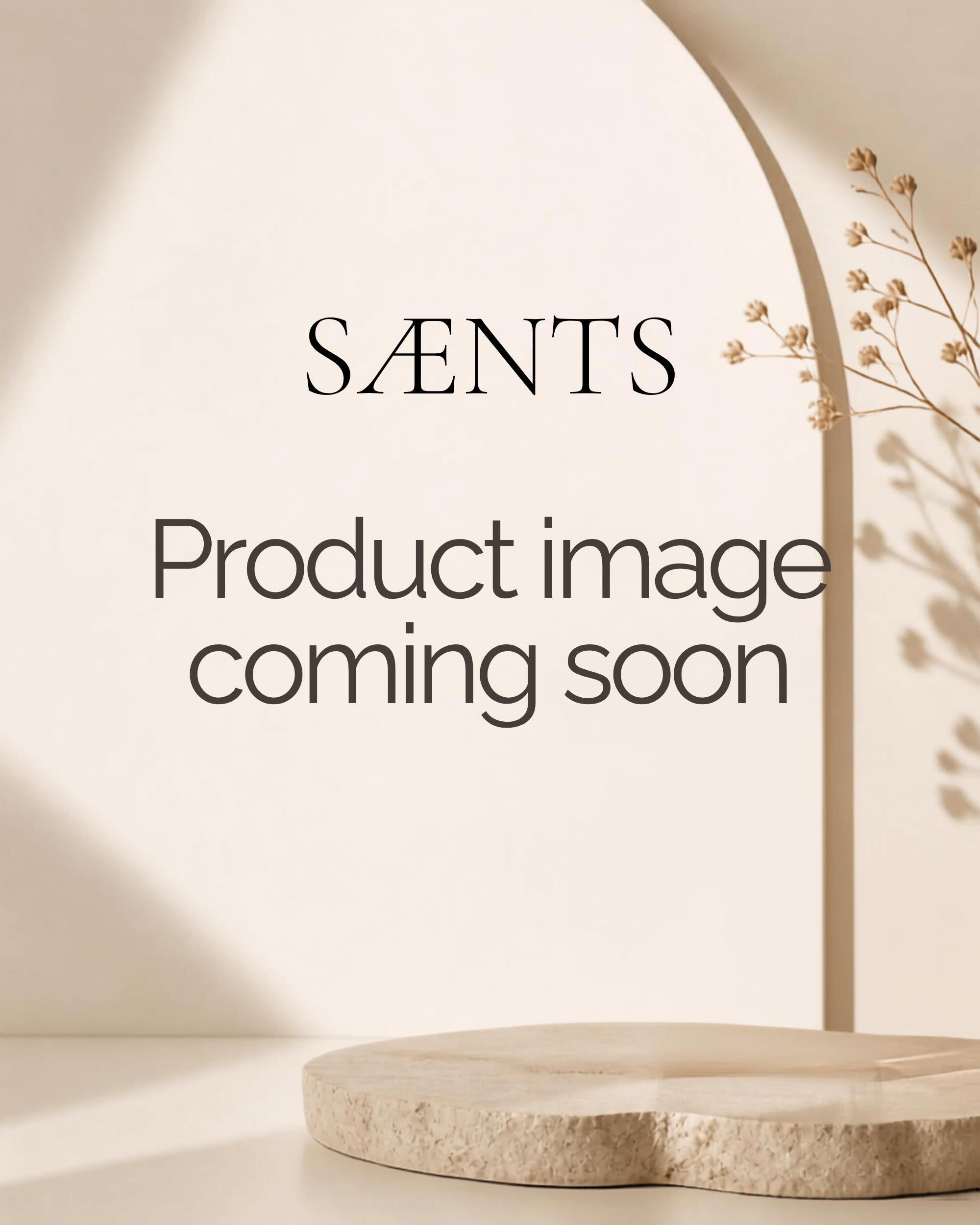 A beige and cream mockup image with the text 'SÆNTS Product image coming soon' displayed in the center, featuring a minimalist archway, soft shadows, and a round stone pedestal at the bottom.